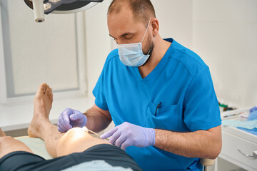 Male doctor in operating room swabs leg of patient lying