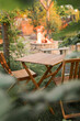 © Olena Butivshchenko - Wooden furniture in the garden against the backdrop of a fire on the patio. Among the branches of the bush stands a wooden table and chairs.