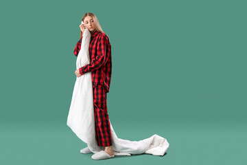 Wall Mural - Sleepy young woman in pajamas with blanket on green background