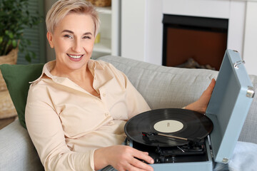 Wall Mural - Mature woman with record player lying on sofa at home