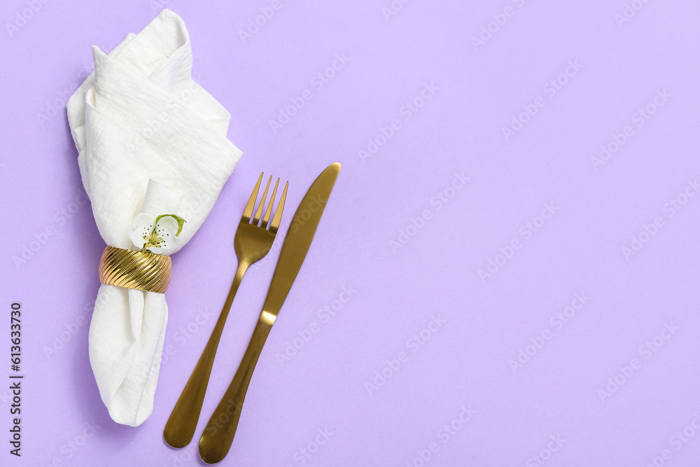 Golden cutlery and folded napkin on lilac background