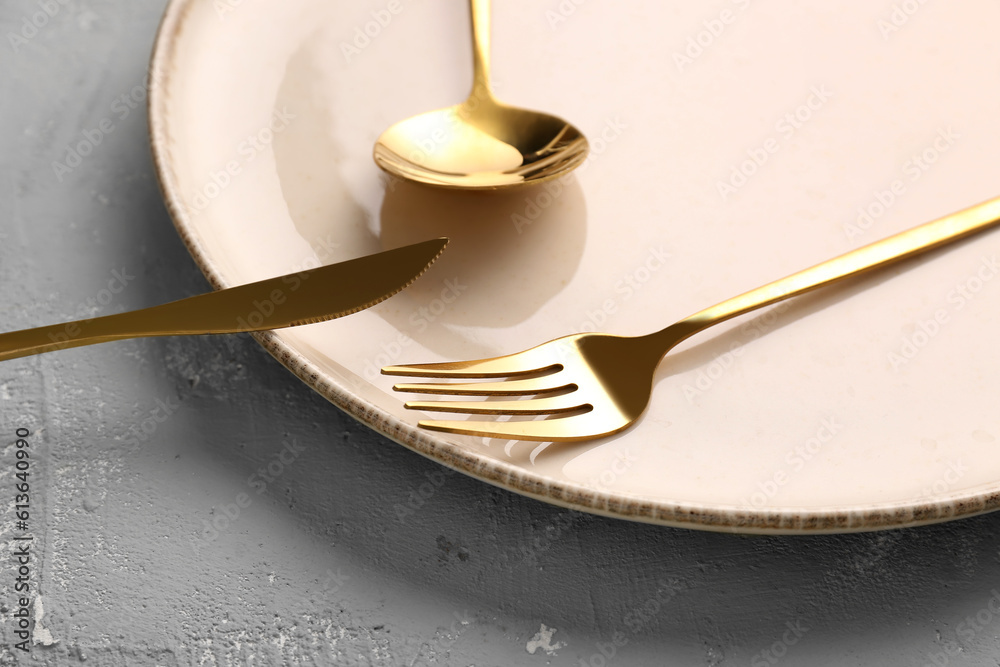 Plate with golden cutlery on grey background