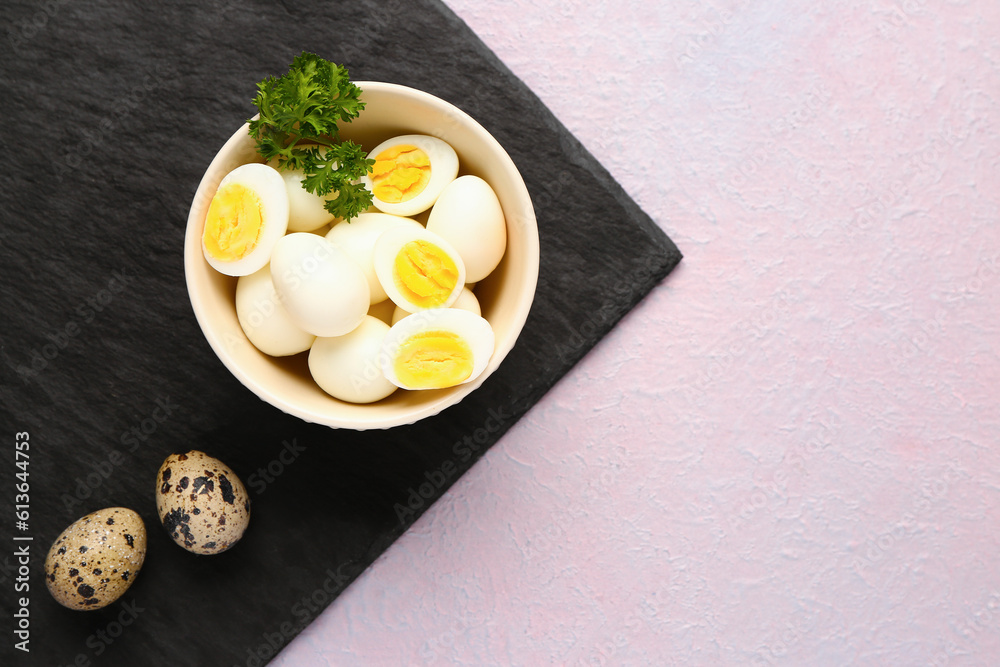 Board with bowl of boiled quail eggs on lilac background
