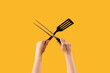 Female hands holding spatula and carving fork on yellow background