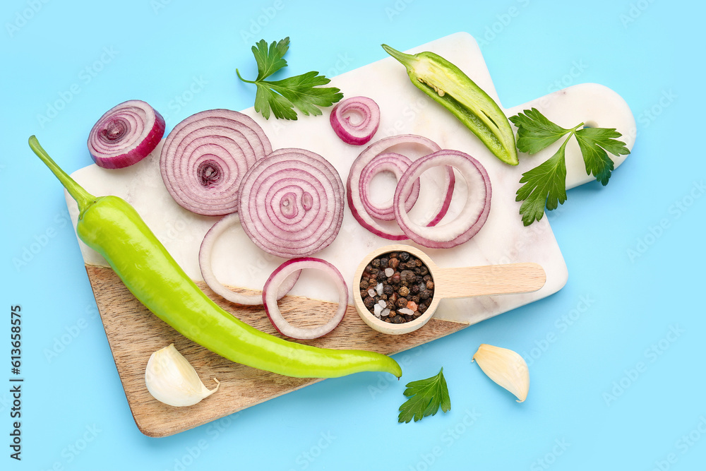 Board with fresh onion slices, jalapeno and spices on blue background