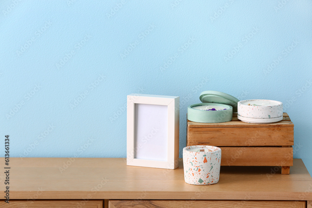 Holders with candles and blank frame on table near blue wall in room