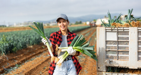 Portrait of positive young woman farmer at large box with harvested fresh leek.