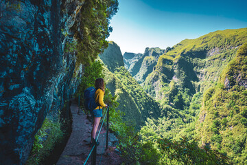 backpacker woman enjoing view from steep cliff jungle hiking trail next to canal through madeiran ra