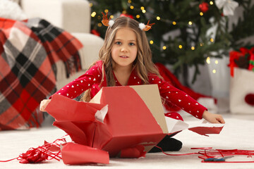 Poster - Cute little girl unwrapping Christmas gift at home