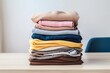 © Kishore Newton - Organized elegance: A stack of clean, freshly laundered women's clothes, including shirts, dresses, and sweaters, neatly folded on a wooden table. Generative AI