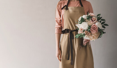 A woman florist in an apron holds in her hands a ready-made delicate wedding bouquet of roses and peonies. Faceless unrecognizable figure closeup, banner