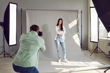 Male photographer shooting model in studio with softboxes and professional photographic equipment. Rare view of photographer taking pictures of female model with digital camera