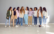 © Studio Romantic - Full size group of a cheerfull happy young diverse women friends or coworkers and company employees looking at each other hugging and smiling together standing on a grey wall background.