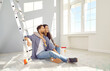 © Studio Romantic - Happy family making their home a cozy place. Young loving couple doing renovations in their house or apartment. Relaxed man and woman sitting on floor with paint bucket, hugging, and smiling