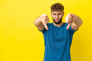 Wall Mural - Young handsome caucasian man isolated on yellow background showing thumb down with two hands