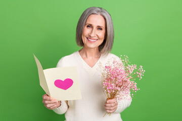 Sticker - Photo of grey hair retired lady reading greetings congratulations postcard hold bouquet gypsophila isolated on green color background