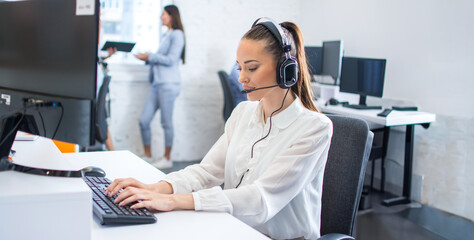 Wall Mural - Beautiful call center worker in headphone working on computer at office.