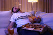Man with chips, pizza and glass of beer sleeping on sofa at night. Bad habit