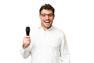 Wall Mural - Brazilian man picking up a microphone over isolated chroma key background with surprise facial expression