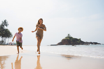 Wall Mural - Beautiful young mother and son run at beach in sunny day and hugging