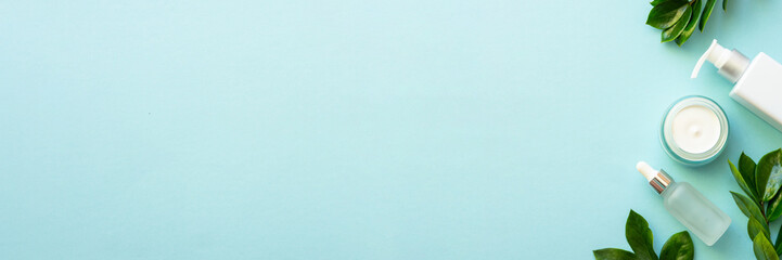 Wall Mural - natural cosmetic products flat lay on blue. cream and serum with green leaves. long banner format.