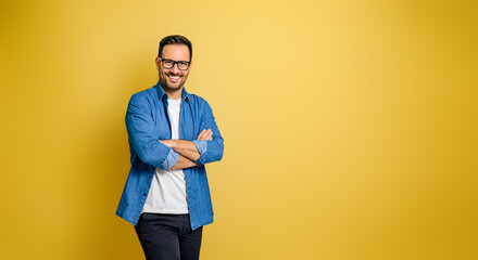 Portrait of confident businessman wearing shirt with arms crossed standing on yellow background
