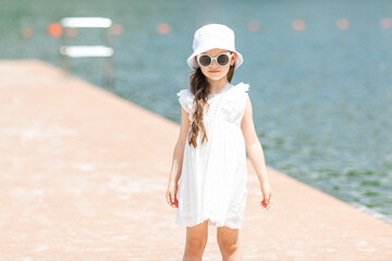 Wall Mural - Happy little girl has fun at wooden pier on the city lake. Summer weekends. Vacation concept.