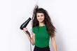 © Budjak Studio - A cute young girl dressed in a green top dries her beautiful long silky hair with a hair dryer against a white background.