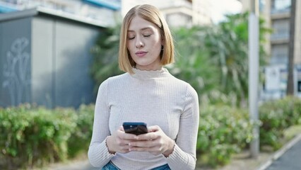 Wall Mural - Young blonde woman smiling confident using smartphone at park