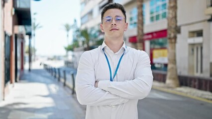 Sticker - Young hispanic man standing with serious expression and arms crossed gesture at street