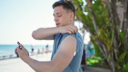 Sticker - Young hispanic man tourist measuring glucose using smartphone and freestyle at seaside