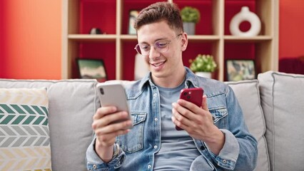 Poster - Young hispanic man using smartphones sitting on sofa at home