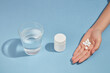 A glass of water, an unlabeled medicine bottle and a handful of pills is arranged in one line on blue background. Medicine, treatments and healthcare