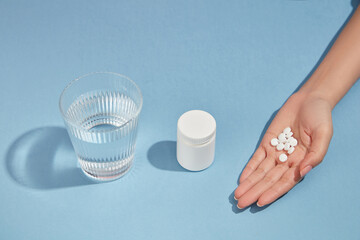 a glass of water, an unlabeled medicine bottle and a handful of pills is arranged in one line on blu