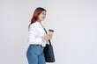 © Mdv Edwards - A smiling young woman with messenger bag standing sideways to the right and holding to-go coffee cup. Isolated on a white background.