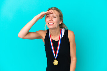 Wall Mural - Young caucasian woman with medals isolated on blue background looking far away with hand to look something