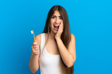 Young caucasian woman brushing teeth isolated on blue background with surprise and shocked facial expression