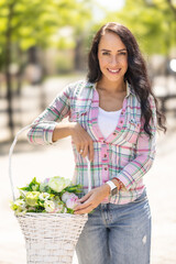 Wall Mural - Beautiful young woman holding a basket with flowers during a sunny day.