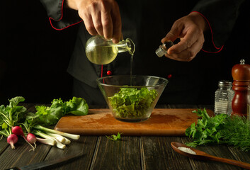 The chef pours olive oil into a bowl of salad. Cooking delicious and healthy food with a set of vitamins in the restaurant kitchen