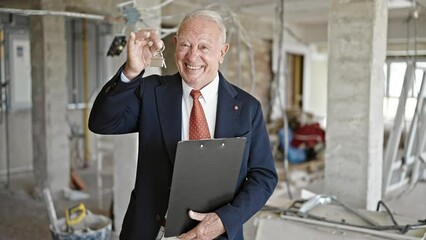 Canvas Print - Senior grey-haired man real state agent holding clipboard and keys of new house at construction site