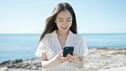 Canvas Print - Young chinese woman using smartphone smiling at seaside