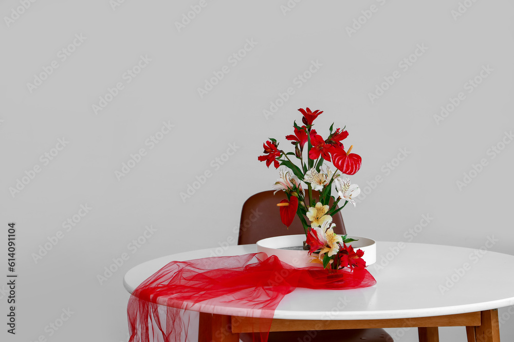 Beautiful ikebana with red veil on dining table in room