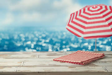 Wall Mural -  Empty wooden table with red tablecloth on table over blurred sea beach background. Summer mock up for design and product display