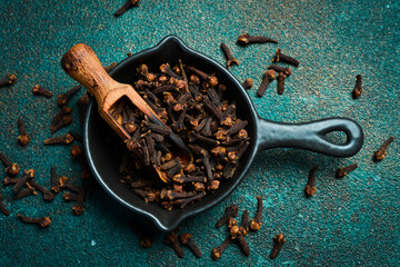 Wall Mural - Cloves in a black bowl. Spices and condiments. Top view. On an old textured background.