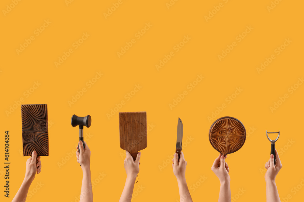 Female hands holding cutting board and different kitchen utensils on yellow background