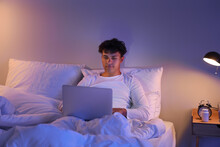 Young man using laptop in bed at night
