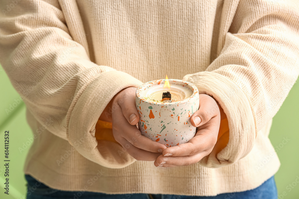 Woman holding burning candle on green background, closeup