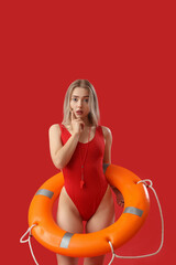 Wall Mural - Thoughtful female lifeguard with ring buoy on red background