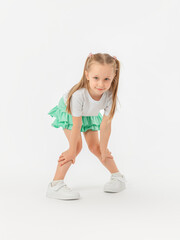 A girl in a T-shirt, sneakers and a green skirt sat down with her hands folded on her knees, looking expressively at the camera on a white background. photo