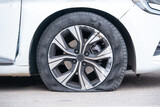 Fototapeta Zwierzęta - Close-up of flat right front wheel of car standing on road with alloy disc. Forced emergency stop on the side of roadside, burst tire, insured event. Broken car waiting tire shop, tire repair service